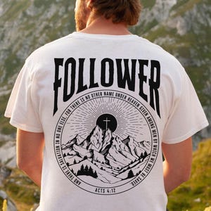Puede incluir: Camiseta blanca con un gráfico negro en la espalda. El gráfico incluye la palabra "FOLLOWER" sobre una escena de montaña con una cruz, rodeada de texto. El texto dice "FOR THERE IS NO OTHER NAME UNDER HEAVEN GIVEN AMONG MEN BY WHICH WE MUST BE SAVED" y "ACTOS 4:12".