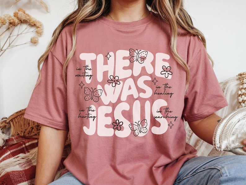 May include: Dusty rose t-shirt with the words "THERE WAS JESUS" in a retro font. The design includes butterflies and flowers. The text "in the waiting, in the hurting, in the healing, in the searching" is also included.