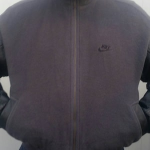 May include: A dark gray zip-up jacket with black leather sleeves and a black Nike logo on the chest.
