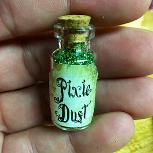 May include: A small glass bottle filled with green glitter and labeled "Pixie Dust". The bottle has a cork stopper and a white label with black lettering.