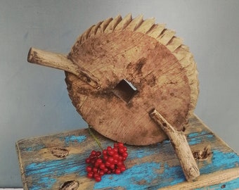 May include: A rustic wooden stool with a blue and white painted top. A wooden wheel with a carved design sits on top of the stool. A small cluster of red berries is on the stool's surface.