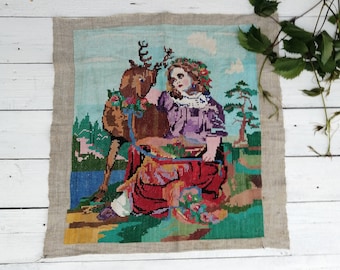 Peut inclure: Une broderie au point de croix représentant une jeune femme avec une couronne de fleurs assise avec un cerf dans un décor de forêt. La femme porte une robe violette et rouge et le cerf est brun avec des bois. L'arrière-plan est un ciel bleu avec des nuages et des arbres verts.