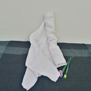 May include: A white cotton muslin cloth is rolled up and laid on a black surface. Three plastic flowers with green stems are on the surface.