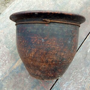 May include: A brown clay pot with a wire rim. The pot has a rustic, aged appearance.