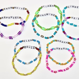 May include: Colorful beaded bracelets featuring names like Snow White, Rapunzel, Tiana, Jasmine, Cinderella, Ariel, Elsa, Belle, Moana, and Aurora. Each bracelet has a different color scheme, with white letter beads spelling out the names.