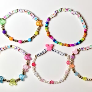 May include: Five colorful beaded bracelets with various phrases, including "MAGIC KINGDOM", "IT'S A SMALL WORLD", "MAKE MAGIC", and "BEST DAY". Each bracelet features a different color scheme and decorative accents.