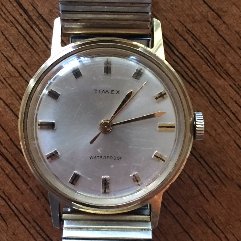 May include: A gold-toned Timex wristwatch with a silver band. The watch face is white with black markings and the words "Timex" and "Waterproof".