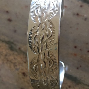 May include: A silver bracelet with a detailed, engraved design of repeating leaf patterns.
