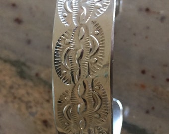 May include: A silver bracelet with a detailed, engraved design of repeating leaf patterns.