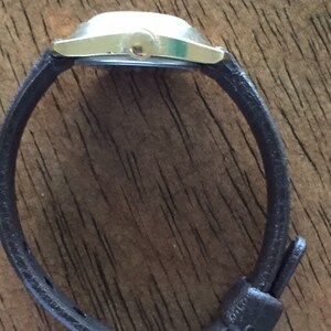 Pu&ograve; includere: Un orologio da polso argentato con un cinturino in pelle marrone e una fibbia argentata.