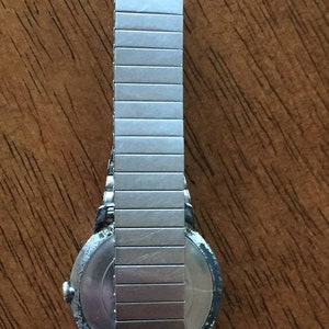 May include: A silver wristwatch with a round face and a metal band. The watch has a silver band with a textured finish.