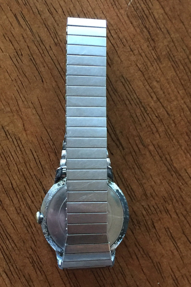 May include: A silver wristwatch with a round face and a metal band. The watch has a silver band with a textured finish.