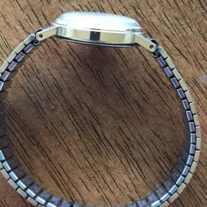 May include: A silver wristwatch with a silver metal band. The watch has a round face and a silver metal case.