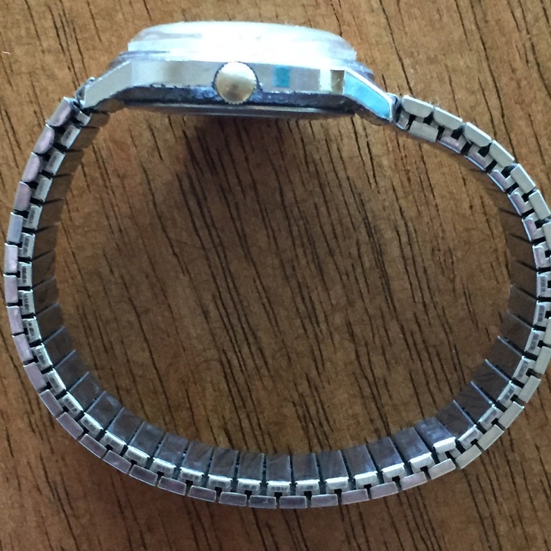 May include: A silver watch with a silver metal band. The watch has a round face and a gold-colored crown.