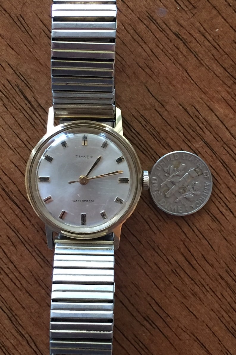 May include: A gold-toned Timex wristwatch with a white face and black hands. The watch has a silver metal band and says "Waterproof" on the face.