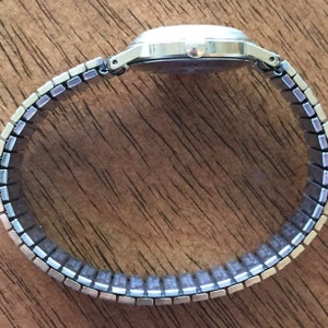 May include: A silver wristwatch with a silver metal band. The band is made of small, rectangular links.