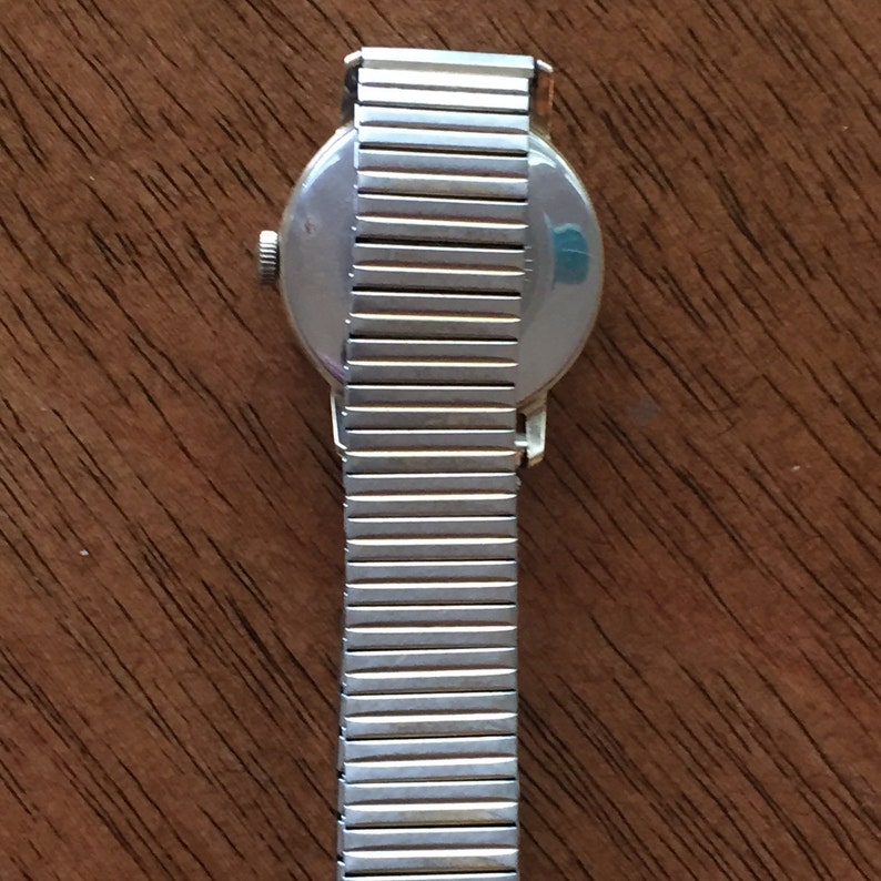May include: A silver wristwatch with a silver metal band. The watch face is round and has a silver rim.