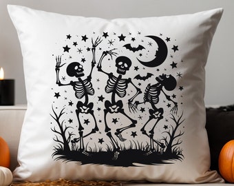 May include: A white square throw pillow featuring a black graphic print of three dancing skeletons in a field with bare trees, stars, a crescent moon, and two bats. The design is centered on the front of the pillow, creating a high-contrast look.