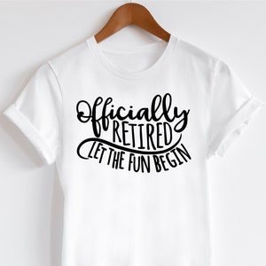 May include: A white t-shirt with the words "Officially Retired Let The Fun Begin" in black script. The shirt is hanging on a wooden hanger.