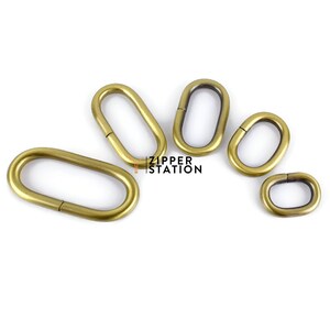 May include: Five oval-shaped metal rings in various sizes. The rings are brass in colour and have a smooth finish. The rings are arranged in a semi-circle.