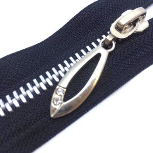 May include: A silver zipper pull with a teardrop shape and two clear rhinestones. The zipper pull is attached to a black zipper tape with white teeth.