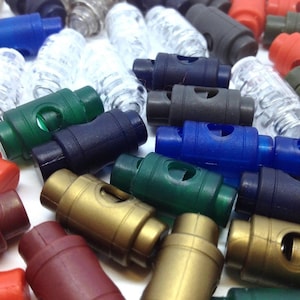 May include: Assortment of colourful plastic toggle clasps in various colours, including red, blue, green, brown, and black. The clasps are used for adjusting the length of straps, cords, or ropes.
