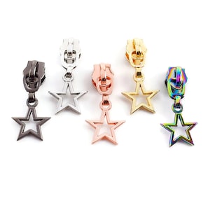 May include: Five zipper pulls with star-shaped charms. The charms are silver, gold, rose gold, black, and rainbow.