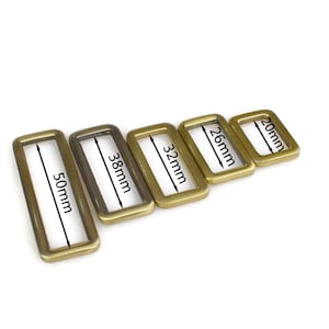 May include: Five gold-toned metal belt buckle slides in different sizes. The slides are arranged from largest to smallest, with the largest slide measuring 50mm, the next largest measuring 38mm, the next measuring 32mm, the next measuring 26mm, and the smallest measuring 20mm.