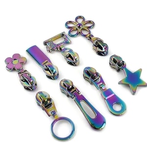 May include: Assortment of colourful zipper pulls in various shapes, including a flower, star, sewing machine, and a circle. The zipper pulls are made of metal and have a rainbow iridescent finish.