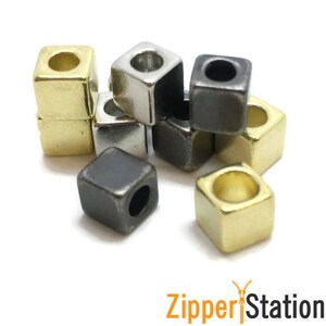 May include: Assortment of square metal zipper pulls in gold, silver, and black. The zipper pulls have a hole in the centre for attaching to a zipper.