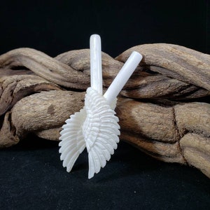 May include: A pair of white, carved, angel wings. The wings are made of a smooth, white material and are intricately detailed. The wings are displayed on a piece of driftwood.