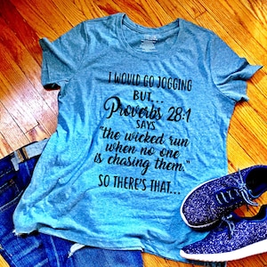 May include: A light blue t-shirt with a black graphic print that says "I would go jogging but... Proverbs 28:1 says "the wicked run when no one is chasing them." So there's that..."