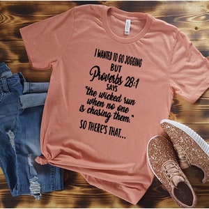 May include: A peach-colored t-shirt with a black graphic print that reads "I wanted to go jogging but Proverbs 28:1 says "the wicked run when no one is chasing them." So there's that..."