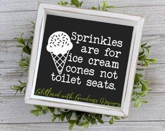 May include: White sign with black background and white text that reads "Sprinkles are for ice cream cones not toilet seats."  The sign also has a white ice cream cone with sprinkles on top.