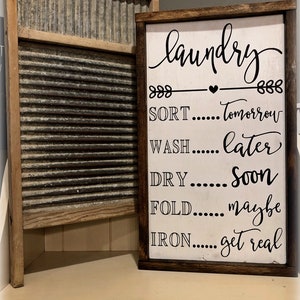 May include: A white wooden sign with a brown frame reads "laundry" with a heart and arrows. The sign lists the laundry tasks with humorous deadlines: "SORT...Tomorrow", "WASH...Later", "DRY...Soon", "FOLD...Maybe", "IRON...Get Real".