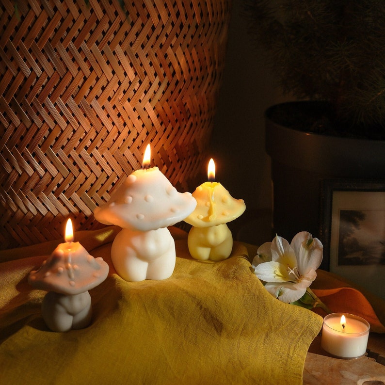 May include: Three mushroom-shaped candles, two white and one yellow, with flames lit. The candles are on a yellow tablecloth with a white flower.