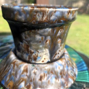 May include: A ceramic planter with a flared top and a wide base. The planter features a glaze with a blend of blue, brown, and white colors. The glaze has a dripped effect, creating a unique pattern. The planter is suitable for small plants.