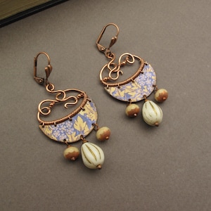 Könnte beinhalten: Ein Paar kupferfarbene Ohrringe mit einem floralen Design in Blau und Gelb. Die Ohrringe haben eine Halbmondform mit Drahtdetails und hängenden Perlen in Creme und Braun.