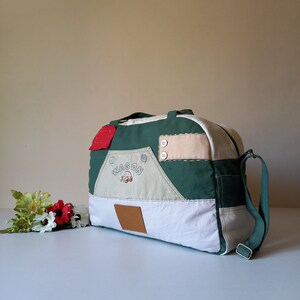 Peut inclure: Un sac de voyage patchwork vert, blanc et beige, avec un accent rouge et un carré en cuir marron. Le sac porte le mot "WAGON" et une illustration de voiture. Il a une bandoulière verte et deux boutons beiges.