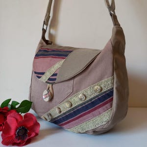 May include: A beige shoulder bag with a flap closure, adorned with striped fabric in red, blue, and beige. The bag features decorative buttons and lace trim. A red flower is in the foreground.