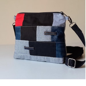 Op de afbeelding: Een patchwork crossbodytas met een zwarte verstelbare riem. De tas heeft een mix van stoffen, waaronder denim, pied-de-poule en effen zwarte en rode panelen. De tas heeft een ritssluiting en zilverkleurige hardware.