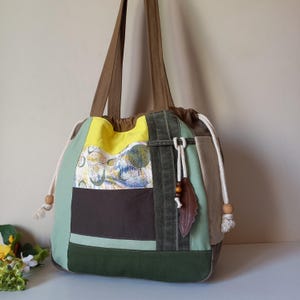 Può includere: Una borsa tote patchwork con chiusura a coulisse. La borsa presenta una varietà di colori, tra cui verde, giallo, marrone e beige. Ha lunghe cinghie marroni e un ciondolo decorativo a forma di foglia di cuoio. La borsa misura circa 38 cm di larghezza e 36 cm di altezza.