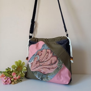 May include: A green, pink and blue patchwork tote bag with a floral design. The bag has a black adjustable strap and a drawstring closure.