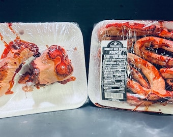 May include: Two packages of raw meat products, one labeled "Mountain Man Meat & Oysters" and the other "Uncle Wilbur's Fresh Chitterlings." Both are wrapped in clear plastic on white foam trays. The meat appears to be red and pink.