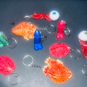 May include: A collection of 10 keychains featuring various anatomical organs and body parts, including a brain, heart, eye, and intestines. The keychains are made of a soft, fleshy material and are painted in realistic colors.