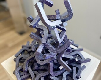 May include: A sculpture made of many small, silver-colored, U-shaped pieces stacked on top of each other. The sculpture is on a white pedestal.