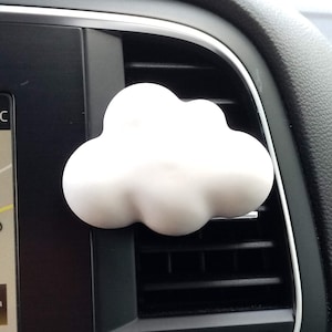 Puede incluir: Un ambientador de coche en forma de nube blanca colgando del respiradero de un salpicadero de coche negro. La pantalla digital del coche muestra una temperatura de 22 grados Celsius.