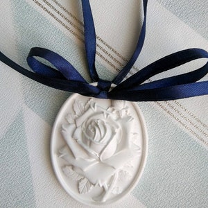May include: White ceramic ornament shaped like a rose with a blue ribbon tied around it.