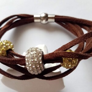 May include: A brown leather wrap bracelet with three round beads. The beads are decorated with clear and yellow rhinestones.