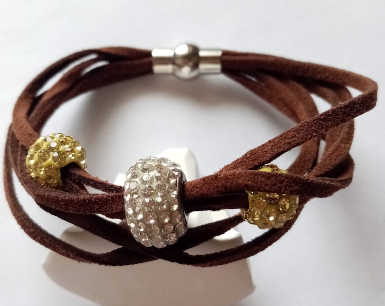 May include: A brown leather wrap bracelet with three round beads. The beads are decorated with clear and yellow rhinestones.